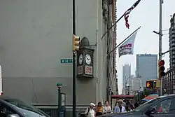 A bronze sign on the eastern end of the 14th Street facade. This sign is triangular and contains a pair of clock faces.