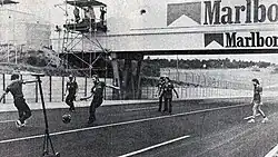 Black-and-white photograph of men playing football on a racetrack