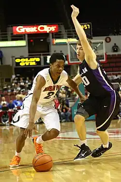 Moore in Morgan Park home white uniform dribbling past a Caucasian player in a black uniform with purple trim with one arm raised in the air.