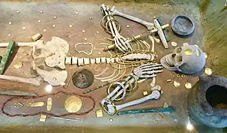 Skeleton in a museum case, with many golden offerings covering and surrounding the body.