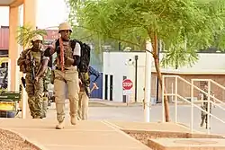 Three soldiers on a pavement in front of a building.