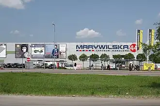 A metal wall of a simple, cuboid building, with mall’s and multiple advertisements