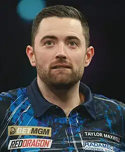 Luke Humphries at a Premier League Darts event, facing straight forward and looking upwards.
