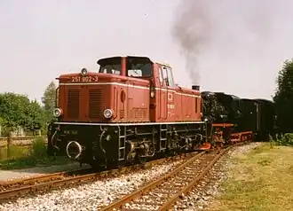 Red two-bogie diesel locomotive with a single off-centre cab and lower bonnets at each end. The nearest bonnet is lower than the other one.