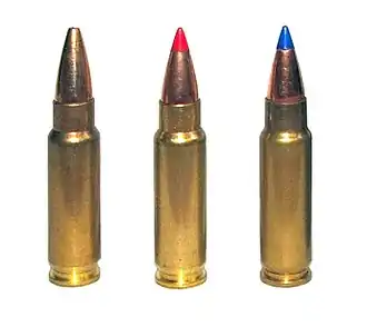 Photo of three 5.7×28mm sporting cartridges. The left cartridge has a plain hollow tip, the center cartridge has a red plastic V-max tip, and the right cartridge has a blue plastic V-max tip.