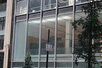 Detail of the second story of the facade. There are tall windows set between vertical steel mullions. Above and below the windows are black spandrel panels. There is a tree in front of the window to the right.