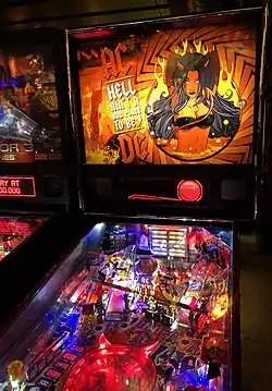 Pinball machine in the style of AC/DC. The artwork shows the AC/DC logo in between the words "Hell Ain't a Bad Place to Be" with the logo's high voltage symbol at the beginning and end of the words, and a hand-drawn woman with long black hair, devil horns and a black bikini, standing in lava with fire in the background.