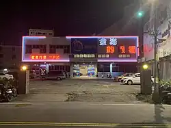 A large indoor shrimp pond building at night, with neon signs in Chinese.