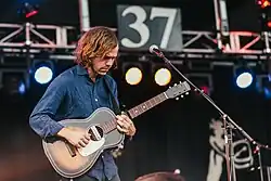 Aaron Dessner in a blue shirt, playing a guitar