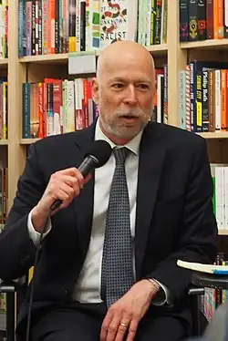 Adam Liptak in a suit and tie, holding a microphone