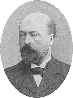 A black and white photograph of a balding bearded man in a suit looking left