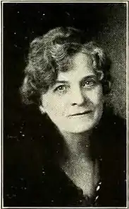 A white woman with greying hair in a curled set style, wearing dark clothes