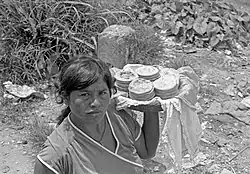 A black-and-white photograph of a woman holding a basket of pupusas