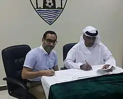 two men sitting at a desk signing papers