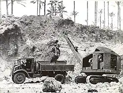 Black and white photo of a mechanical digger dropping soil into the tray of a truck