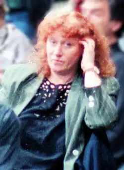 Red-headed woman in a green jacket and blue lace top