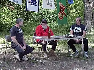 Three middle-aged white men sitting at a camping table outdoors