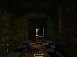 A long, darkened stone hallway with a light at the far end, against which a figure is silhouetted. Carpet is placed down the middle of the black-and-white tiled floor, and a black object protrudes from the bottom right corner of the image.