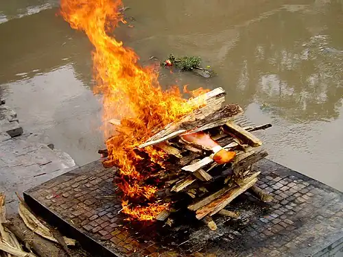 A Hindu cremation rite in Nepal. The samskara above shows the body wrapped in saffron red on a pyre.