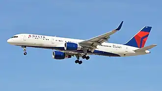 A mostly white Boeing 757 with blue and yellow trim preparing for landing against a grey sky.