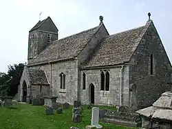A stone church seen from the southeast, showing the chancel, beyond which is a nave with a higher roof and a porch and, beyond that, a tower with a saddleback roof