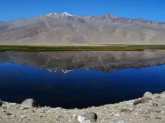 Image of Bukunkul lake taken from the shoreline, with the Pamir mountains reflecting on the surface of the lake.