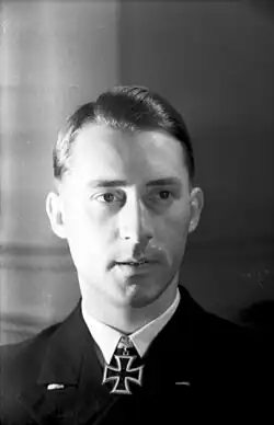 A young man with a black uniform and an Iron Cross at his neck; his hair is combed back.
