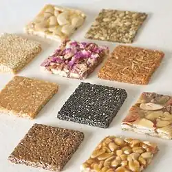 Ten flat squares of chikki. The different colors and textures are due to each square being made from a different type of nut or seed.