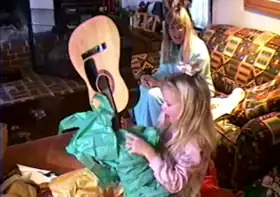 Taylor Swift unwrapping her gift to find a guitar.