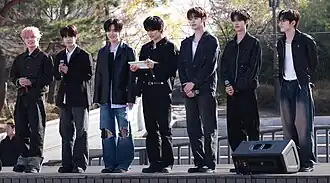 The seven members of Close Your Eyes standing on an outdoor stage