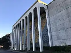 A large building with marble columns. A colorful, abstract mural is visible behind the columns.
