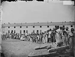 A contraband school, held outdoors at Freedman's Village in Arlington County, Virginia. Note teacher, in coat and tie, on mound at left.