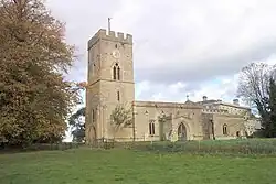 A stone church seen from the south, with a tower surmounted by a battlemented parapet on the left, and the nave with a porch and the chancel to the right