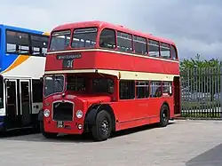 Red half-cab double-decker bus, painted with two cream bands between both decks and with a white-on-black destination display reading '30' to 'Whitehaven', parked in a bus depot