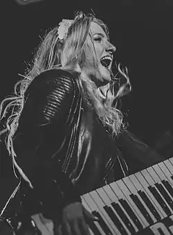 Black and white image of Dana Jean Phoenix holding a keyboard strapped around her neck, appearing to sing