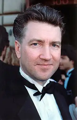 Portrait of David Lynch, a white middle-aged man, with short hair, a shaved beard and blue eyes, wearing a suit, during the 1990 Emmy Awards.