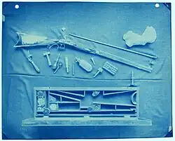 cyanotype image showing a gun and assorted accessories
