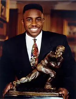 A picture of Desmond Howard with Heisman Trophy statuette.