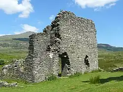 The west tower of the castle, looking north. The tower is craggy and ruined, and a mountain is visible in the distance.