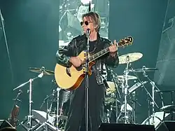 Jacques Dutronc singing on stage in a dark suit, holding a microphone