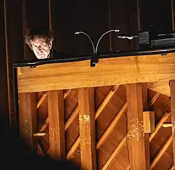 A man's head looking out from behind an upright pinao.