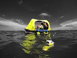 An EPIRB floating in the water next to distressed boating family in a liferaft