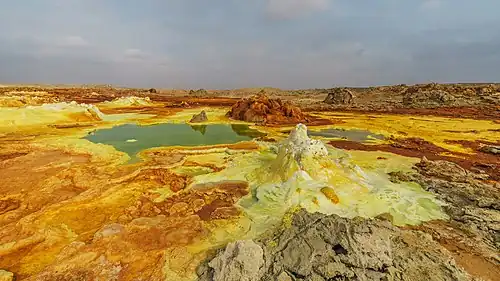 Image 7 Dallol Photograph credit: Alexander Savin Dallol is a cinder-cone volcano in the Danakil Depression, northeast of the Erta Ale Range in Ethiopia. The area lies up to 120 m (390 ft) below sea level, and has been repeatedly flooded in the past when waters from the Red Sea have inundated it. The Danakil Depression is one of the hottest places on Earth, and the evaporation of seawater after these flooding episodes produced thick deposits of salt, as seen in this landscape. The deposits at Dallol include significant quantities of the carbonate, sulfate and chloride salts of sodium, potassium, calcium and magnesium. Hot springs discharge brine to form the blueish ponds, and small, temporary geysers produce cones of salt. More selected pictures