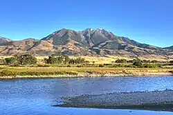 A river flows through a flat valley with mountains in the background.