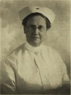 B&W portrait photo of a woman wearing a white nurses hat and uniform.