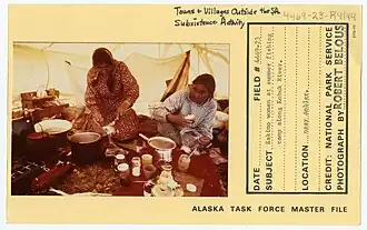 Alaskan park services slip showing two women preparing and storing fish at a summer fishing camp along the Kobuk river. They have many pots and jars out on a table to prepare their fish.
