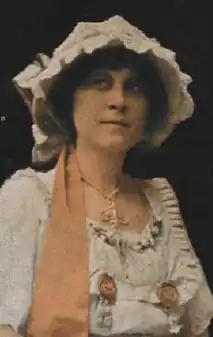Fleta Jan Brown, a white woman, in white dress and hat with orange trim.