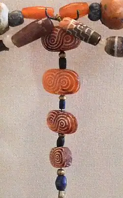 Four oval-shaped carnelian beads with guilloché pattern and one cylindrical bead with stepped pattern (top right) found in Susa excavations, Akkadian Empire or Ur III period. The carnelian is most probably from the Indus region, but the designs are typically Near-Eastern.[41][30]