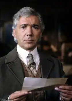 Caucasian male with silver wavy hair dressed in period (Victorian) style of tweed jacket with non-matching waistcoat and tie