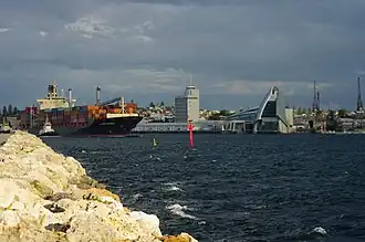 Container ship leaving port. Tall building at centre houses port administration offices. Western Australian Maritime Museum is to the right.